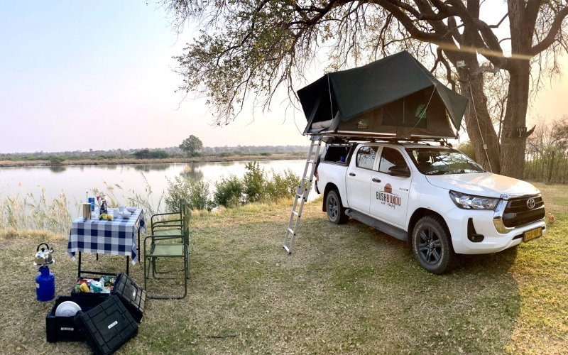 bushbundu-car-rental-windhoek-namibia-side-side-image-of-toyota-hilux-with-pitched-tent-on-the-roof-near-a-lake